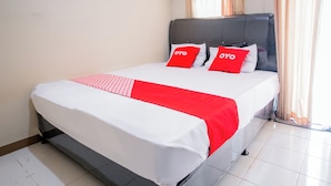 Ein Bett mit weißer und roter Bettdecke, zwei rote Kissen mit dem Aufdruck "OYO" und ein grauer Kopfteil.
