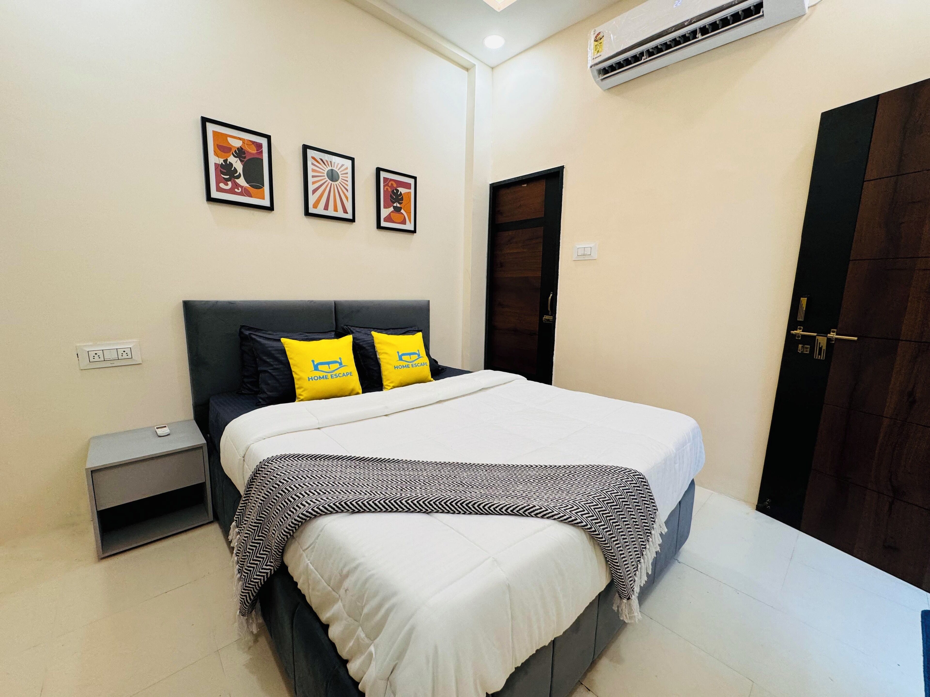 A bedroom with a bed, bedside table, wall-mounted air conditioning unit, and a door.