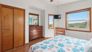 Ein Schlafzimmer mit Bett, Schminktisch, Sessel, Deckenventilator, Fernseher und großen Fenstern mit Blick.
