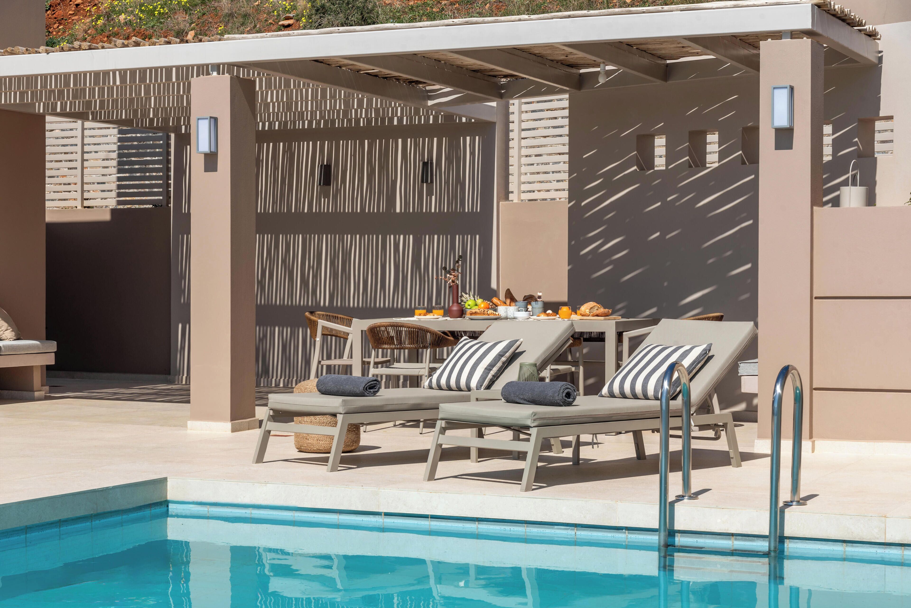 A poolside area with lounge chairs and a table, a covered seating area, and a pool.