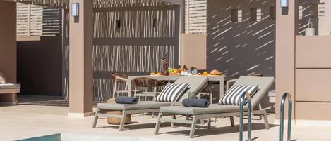 A poolside area with lounge chairs and a table, a covered seating area, and a pool.