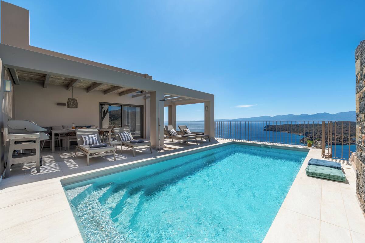 Un espace piscine extérieur moderne, doté de chaises longues et offrant une vue sur la mer.