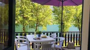 Ein Balkon mit Tisch und Stühlen, einem violetten Sonnenschirm und Blick auf Bäume und Wasser.