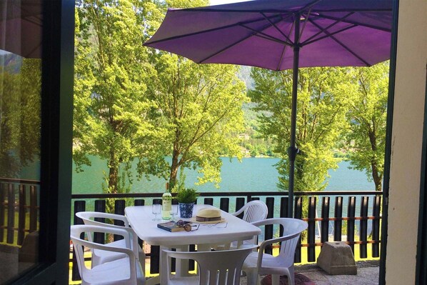 A balcony with a table and chairs, a purple umbrella, and a view of trees and water.