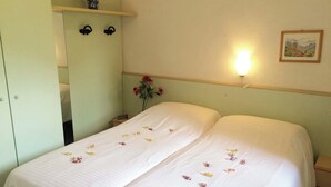 Ein Doppelbett mit weißer Bettdecke und verstreuten Blütenblättern, ein Nachttisch mit Blumenvase, eine Wandleuchte und ein gerahmtes Bild an der Wand.
