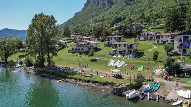Ein Dorf am See mit Häusern, Booten und einer Bergkulisse im Hintergrund.