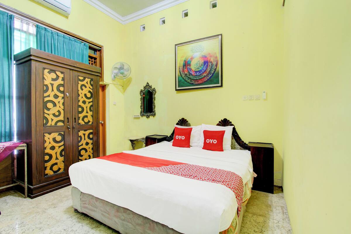 A hotel room with a bed, a wardrobe, a wall-mounted artwork, and a bedside table.