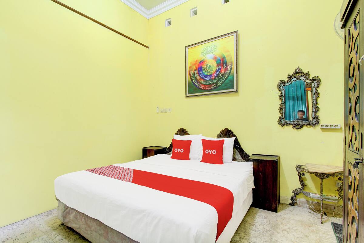 A hotel room with a bed, a painting, a mirror, and a wooden cabinet.