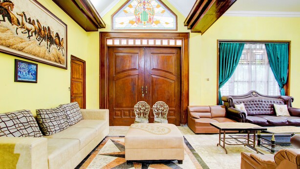 A spacious living room with a large wooden door, a sofa set, a coffee table, and a patterned rug. - Hotel O Homestay Ndalem Kademangan (Ngaglik)