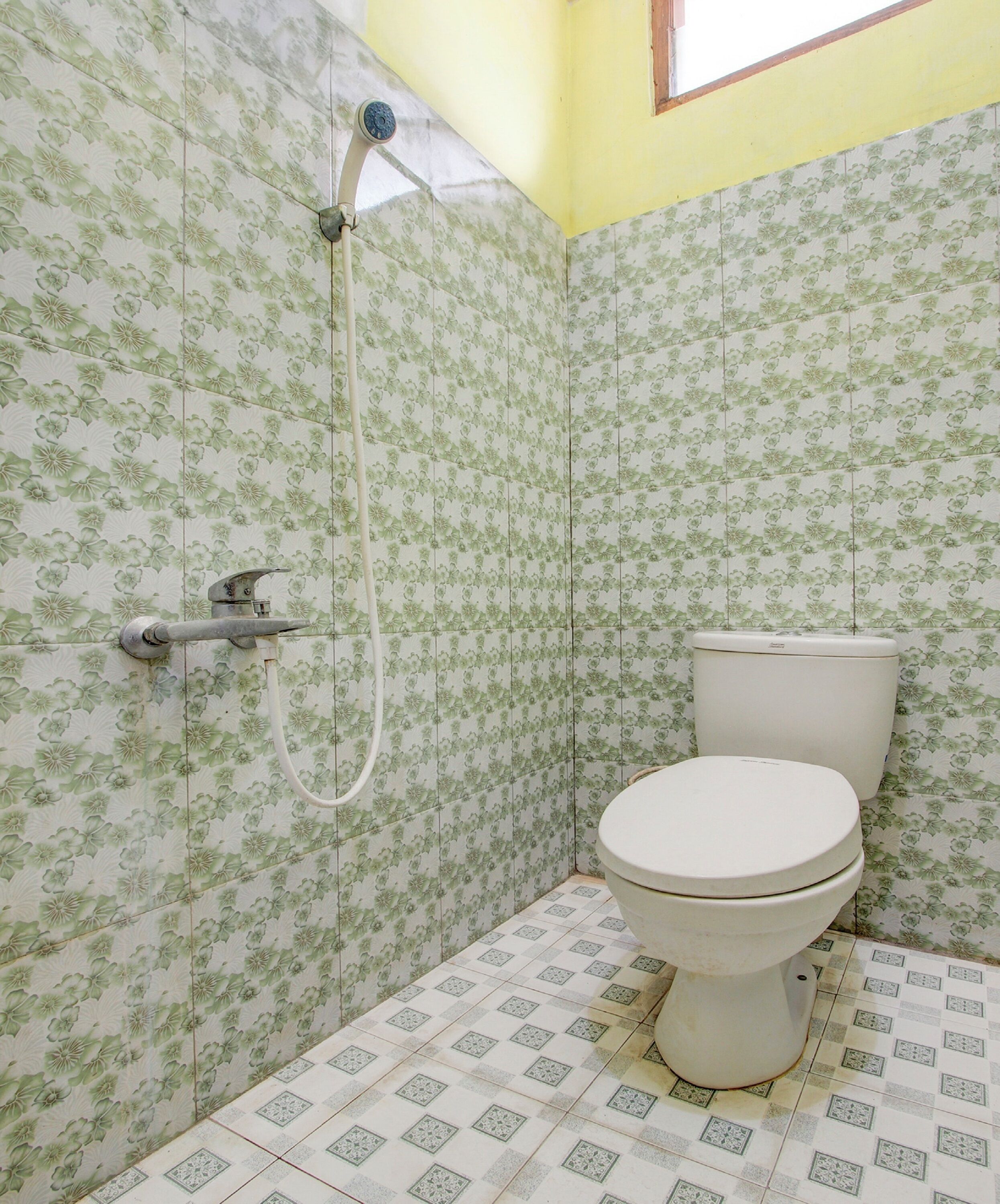 A bathroom with floral patterned tiles, a white toilet, and a shower with a hose.