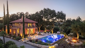 Una casa de dos pisos con piscina, mobiliario exterior y un jardín bien cuidado.