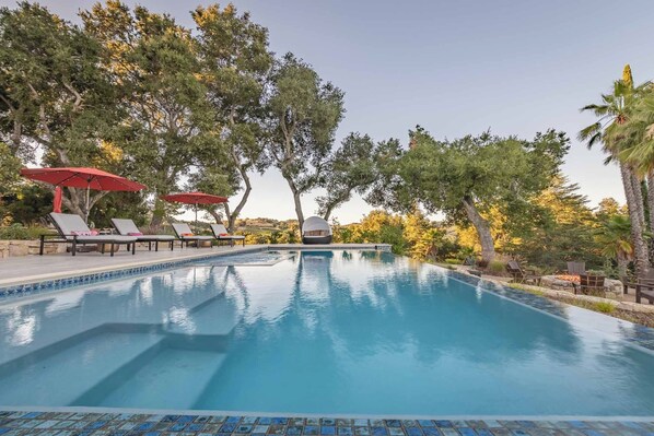 Relax by the serene pool surrounded by lush trees and comfortable lounge chairs.