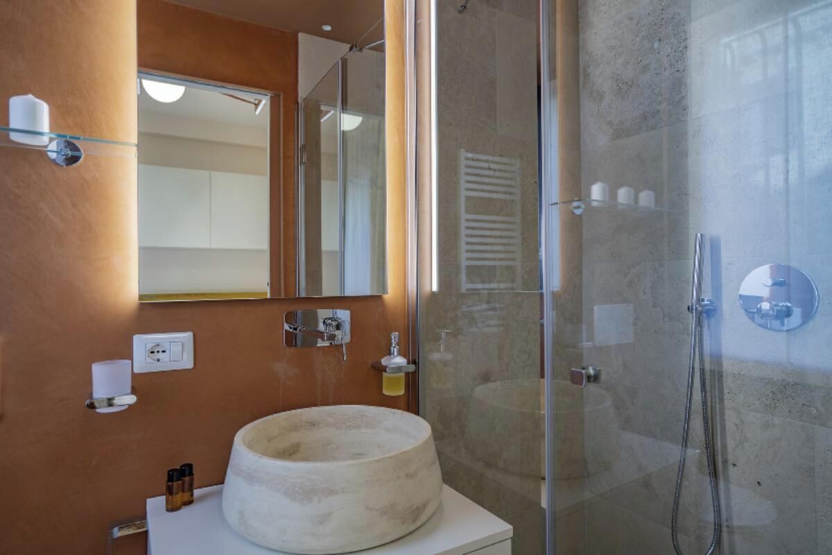A modern bathroom with a round sink, a glass shower enclosure, and a mirror above the sink.