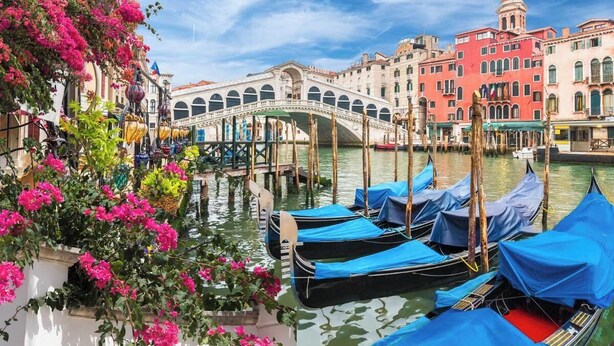 A canal with gondolas docked, a bridge, and historic buildings.