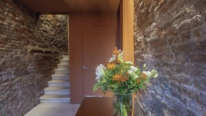 A hallway with a brick wall, a wooden door, and a staircase leading to another room.