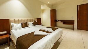 A hotel room with a large bed, wooden headboard, a desk, and a wardrobe. - Patel Comforts Inn & Suites (Mysore)