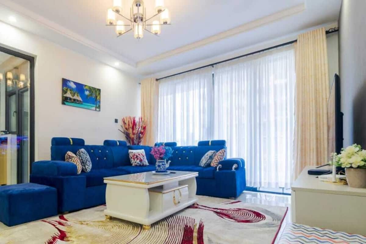 Una sala de estar moderna con un sofá azul, una mesa de centro blanca y una cocina visible a través de un mamparo de vidrio.
