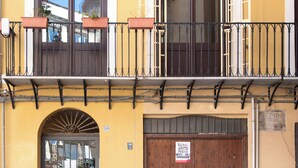 Ein gelbes Gebäude mit einer Holztür, einem Balkon mit Metallgeländern und einem Fenster, das eine Kuppelstruktur reflektiert.