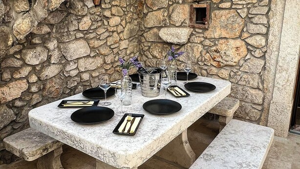 An outdoor dining area with a stone wall backdrop, a marble table, and benches. - Old house Njivice (Omisalj)