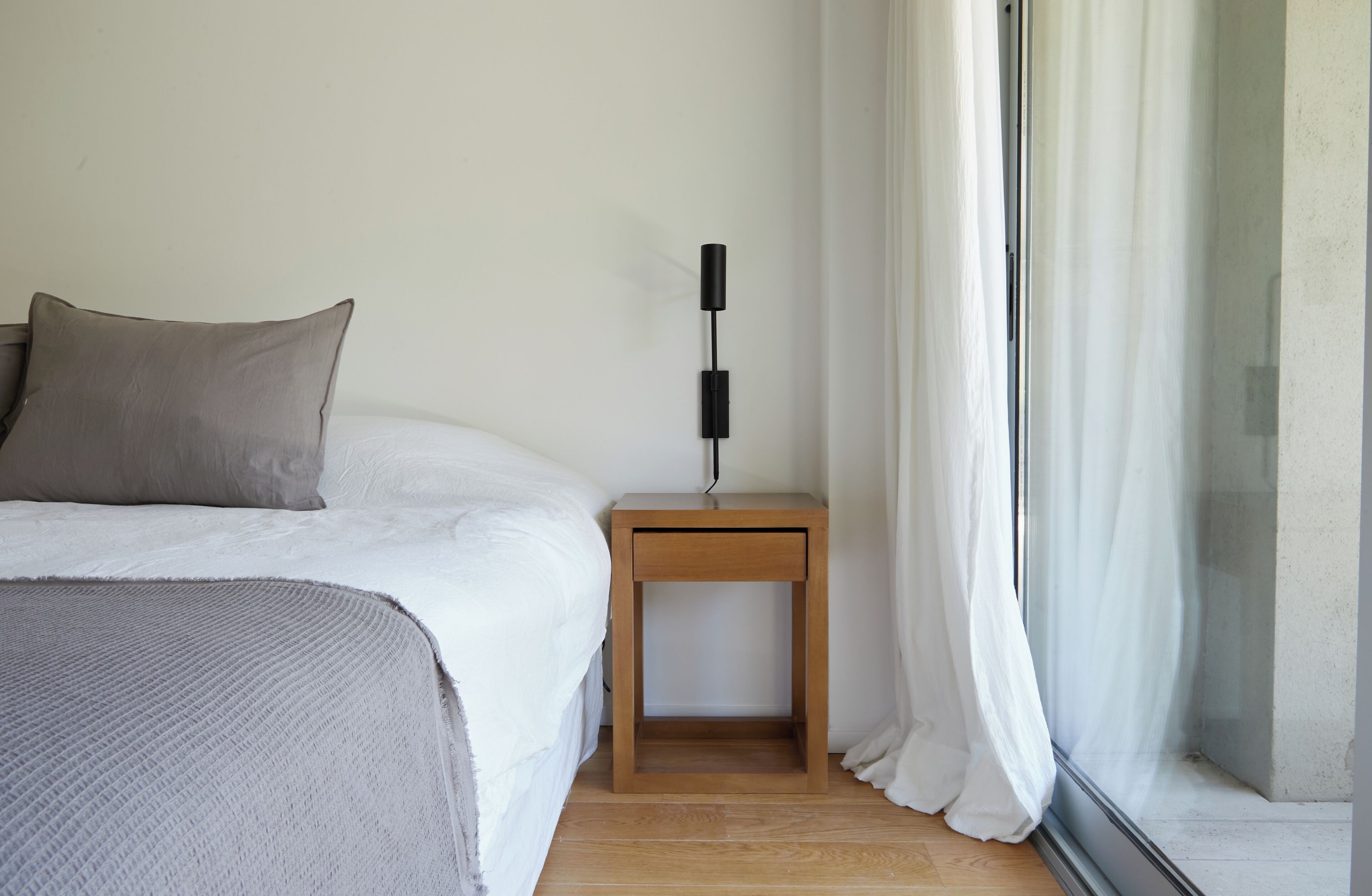 A bedroom with a bed, a bedside table, a lamp, and a window with curtains.