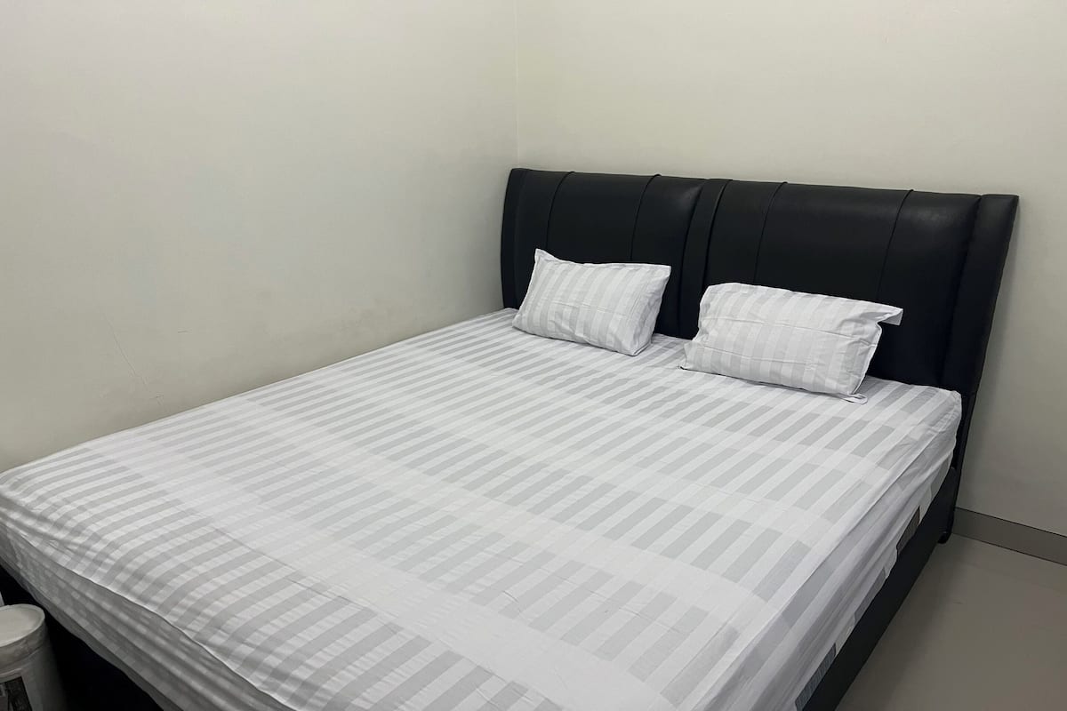 Una cama individual con cabecera negra y ropa de cama a rayas blancas.