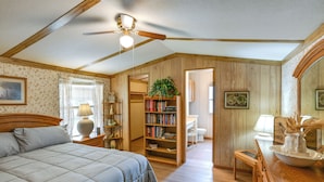 A bedroom with a bed, a wooden headboard, a ceiling fan, a bookshelf, a desk, and a mirror. - Blackwell Home w/ Enclosed Porch: Steps to Water! (Blackwell)