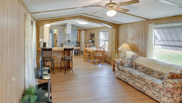 A spacious room with a wooden floor, a ceiling fan, a dining area with a table and chairs, and a sofa with a floral pattern. - Blackwell Home w/ Enclosed Porch: Steps to Water! (Blackwell)