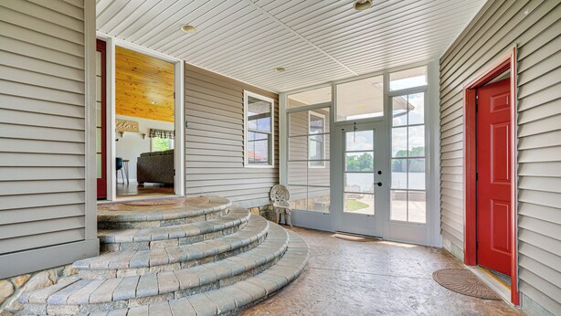 A covered porch with stone steps leading to a door, a red door, and a view of the outdoors. - Lakefront Vacation Rental ~ 10 Mi to Shipshewana! (Howe)