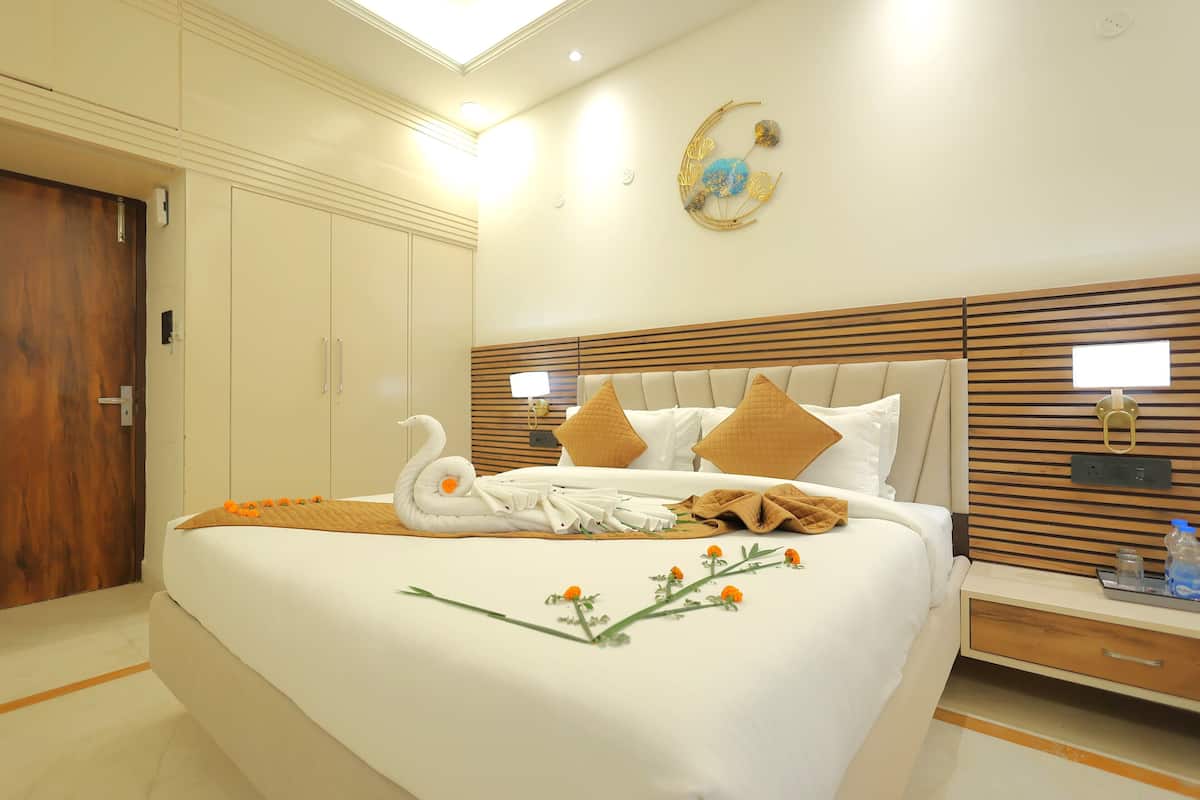 A hotel room with a large bed, a wooden headboard, a nightstand with a lamp, and a wall-mounted TV.