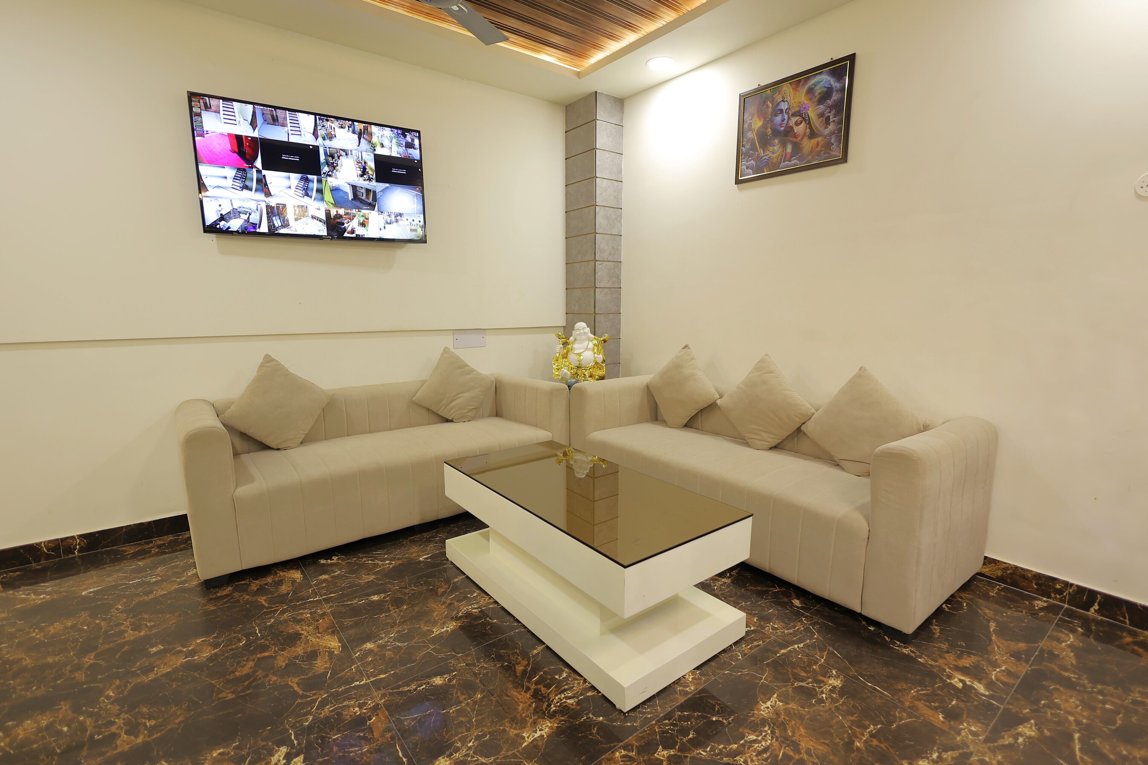 A modern living room with a glass coffee table, beige sofas, and a large flat-screen TV mounted on the wall.