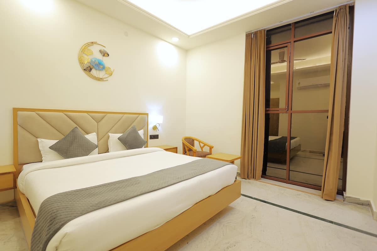 A hotel room with a large bed, a bedside table, a chair, a desk, and a sliding glass door to a balcony.