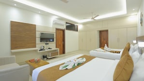 A hotel room with two beds, a TV, a desk, and a ceiling fan. - Shree radha heritage (Haridwar)