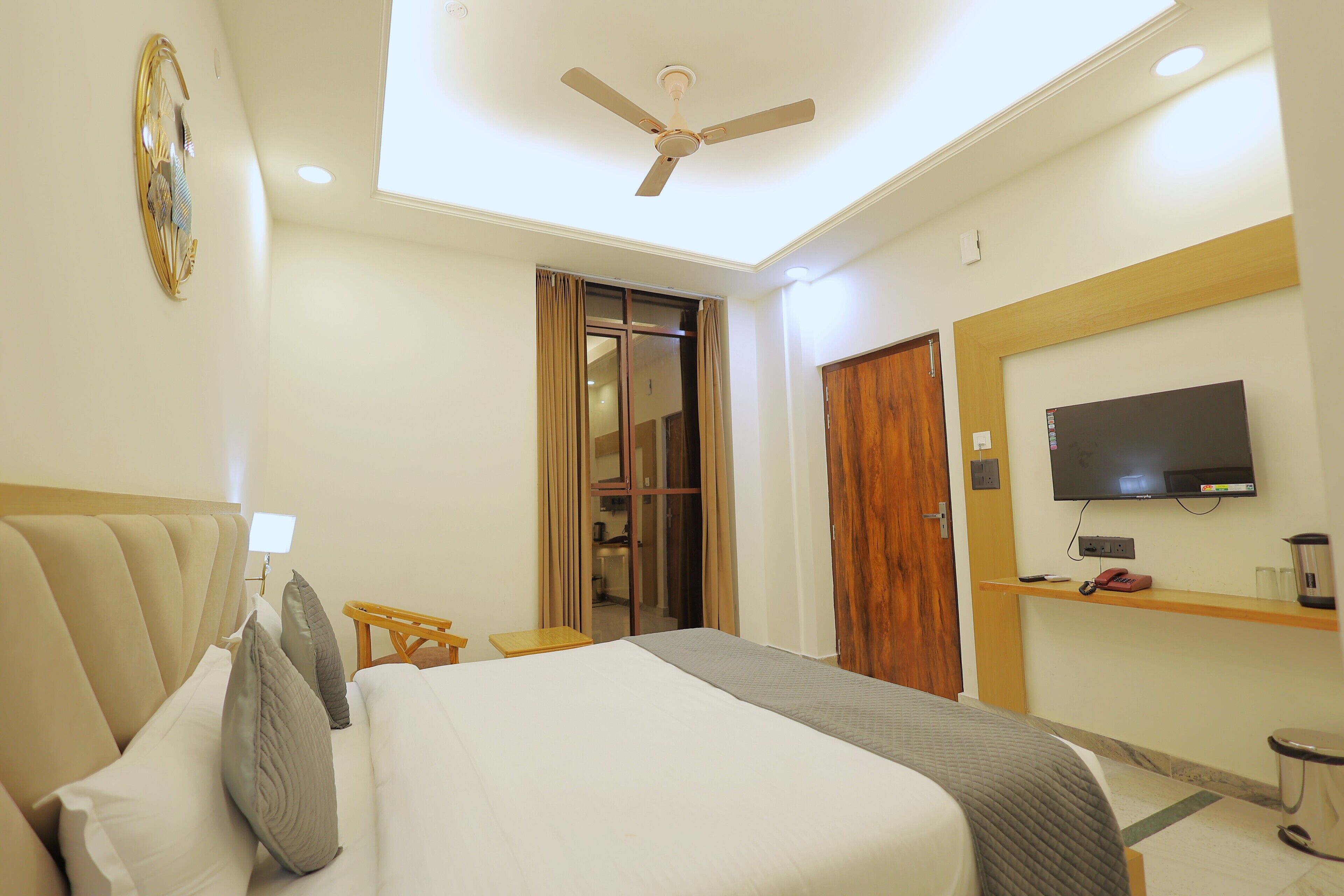 A hotel room with a bed, a ceiling fan, a television, a wooden door, and a small table.