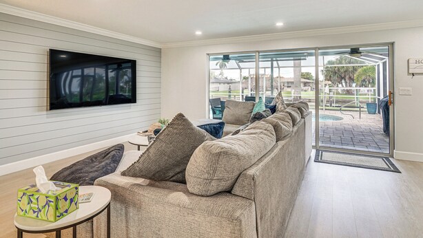 A living room with a sofa, a television mounted on the wall, and a sliding glass door leading to an outdoor patio. - 2 Mi to Beach: Canalfront Home in Cape Coral (Cape Coral)