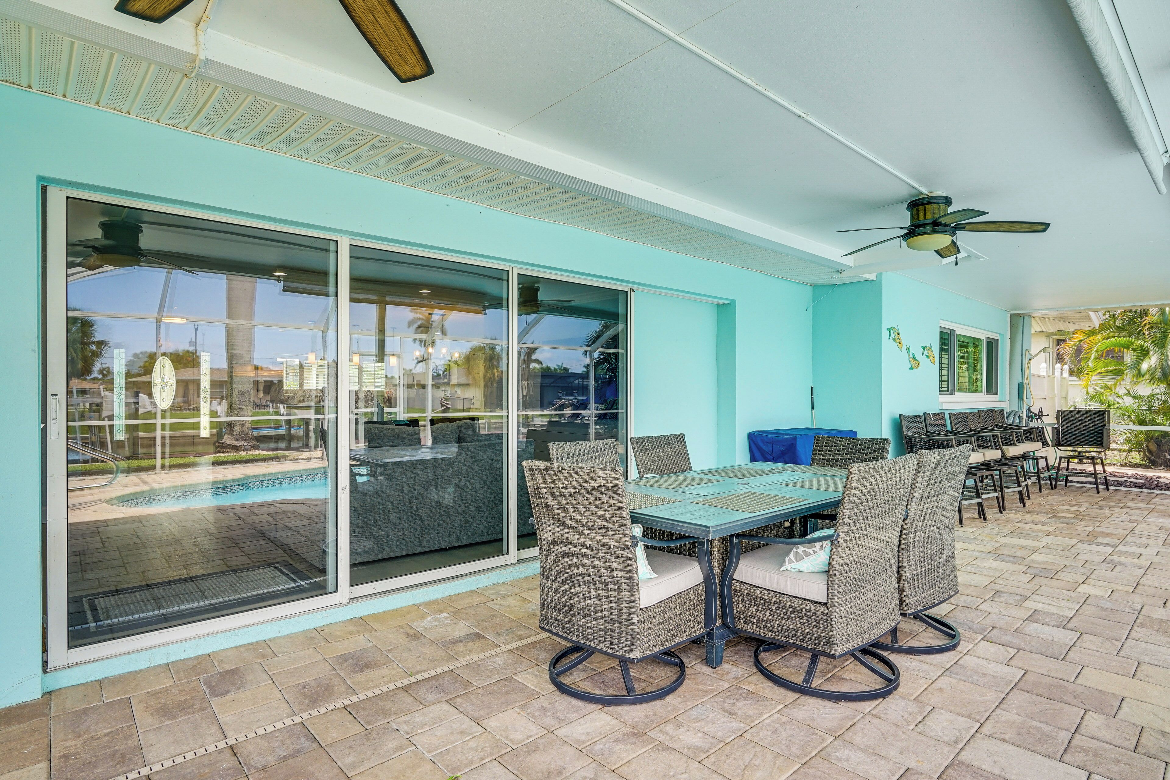 A covered patio with a glass door leading to a pool, outdoor furniture, and ceiling fans.