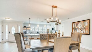 A dining area with a wooden table and upholstered chairs, a chandelier, and a kitchen in the background. - 2 Mi to Beach: Canalfront Home in Cape Coral (Cape Coral)