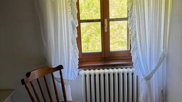 Une pièce avec une chaise en bois, une fenêtre ornée de rideaux blancs et un radiateur placé sous la fenêtre.