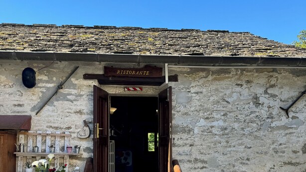 A rustic entrance with a wooden staircase leading to a dark interior, a sign reading "RISTORANTE" above the door, and a rustic wall with a shelf of potted plants. - Albergo Ristorante Ca' di veroli (Bagno di Romagna)