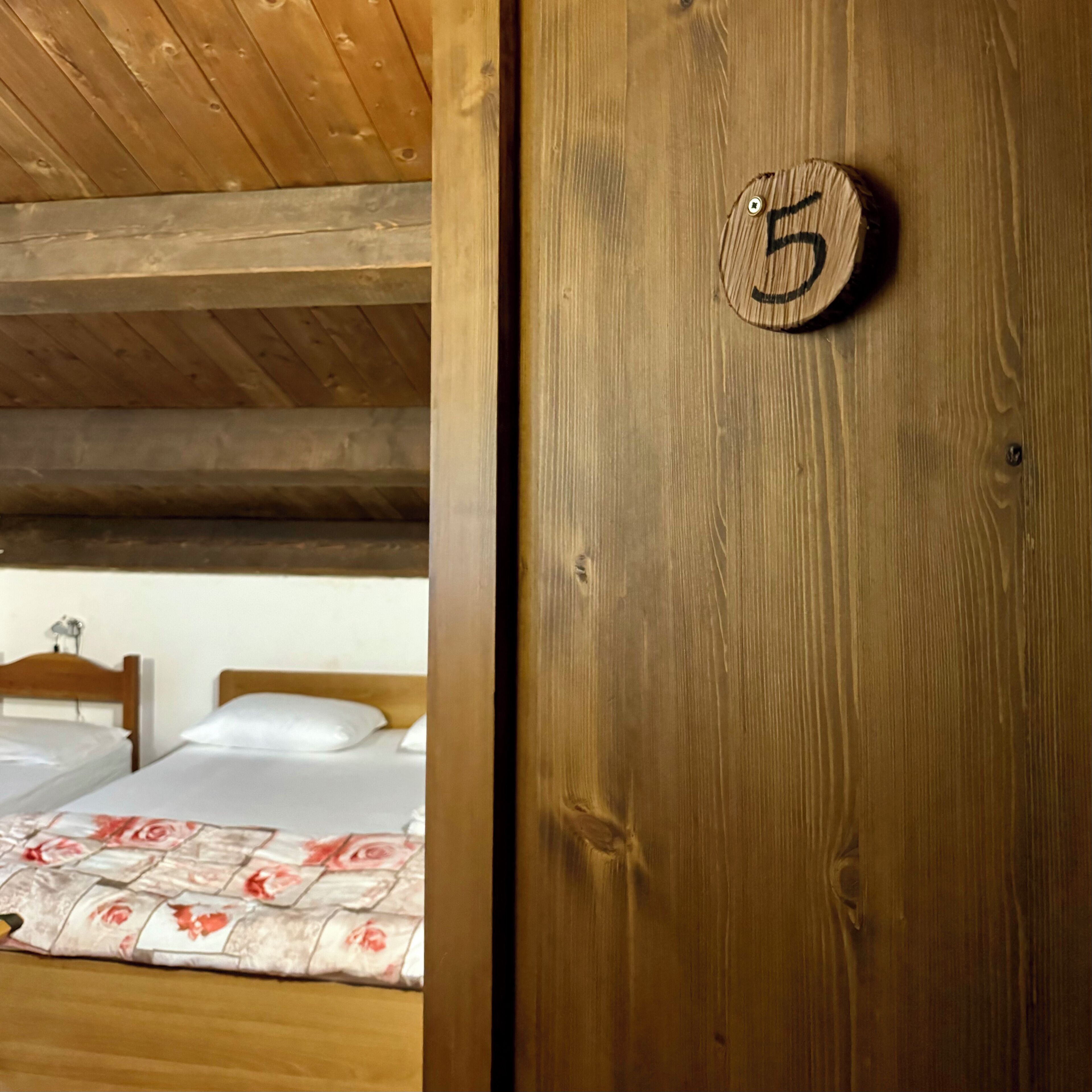 Una puerta de madera con una placa de número, una cama con colcha estampada de flores y un techo de madera.