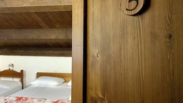 Una puerta de madera con una placa de número, una cama con colcha estampada de flores y un techo de madera.