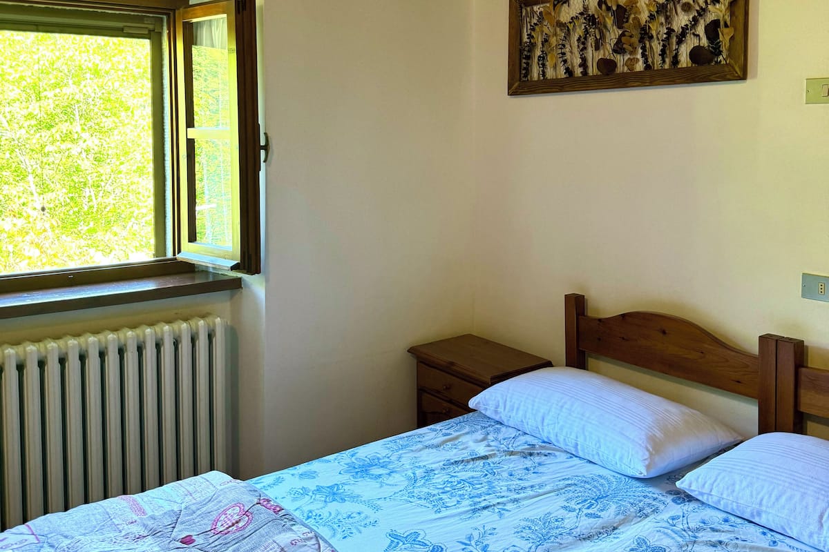 A bedroom with a bed, a nightstand, a window, and a wall-mounted artwork.