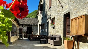 A stone building with a wooden door and window shutters, outdoor seating, and a potted plant. - Albergo Ristorante Ca' di veroli (Bagno di Romagna)