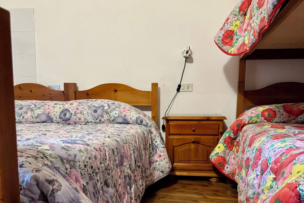 A room with two wooden beds, each with floral bedding. There is a wooden nightstand with a power outlet between the beds.