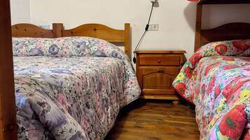 A room with two wooden beds, each with floral bedding. There is a wooden nightstand with a power outlet between the beds.