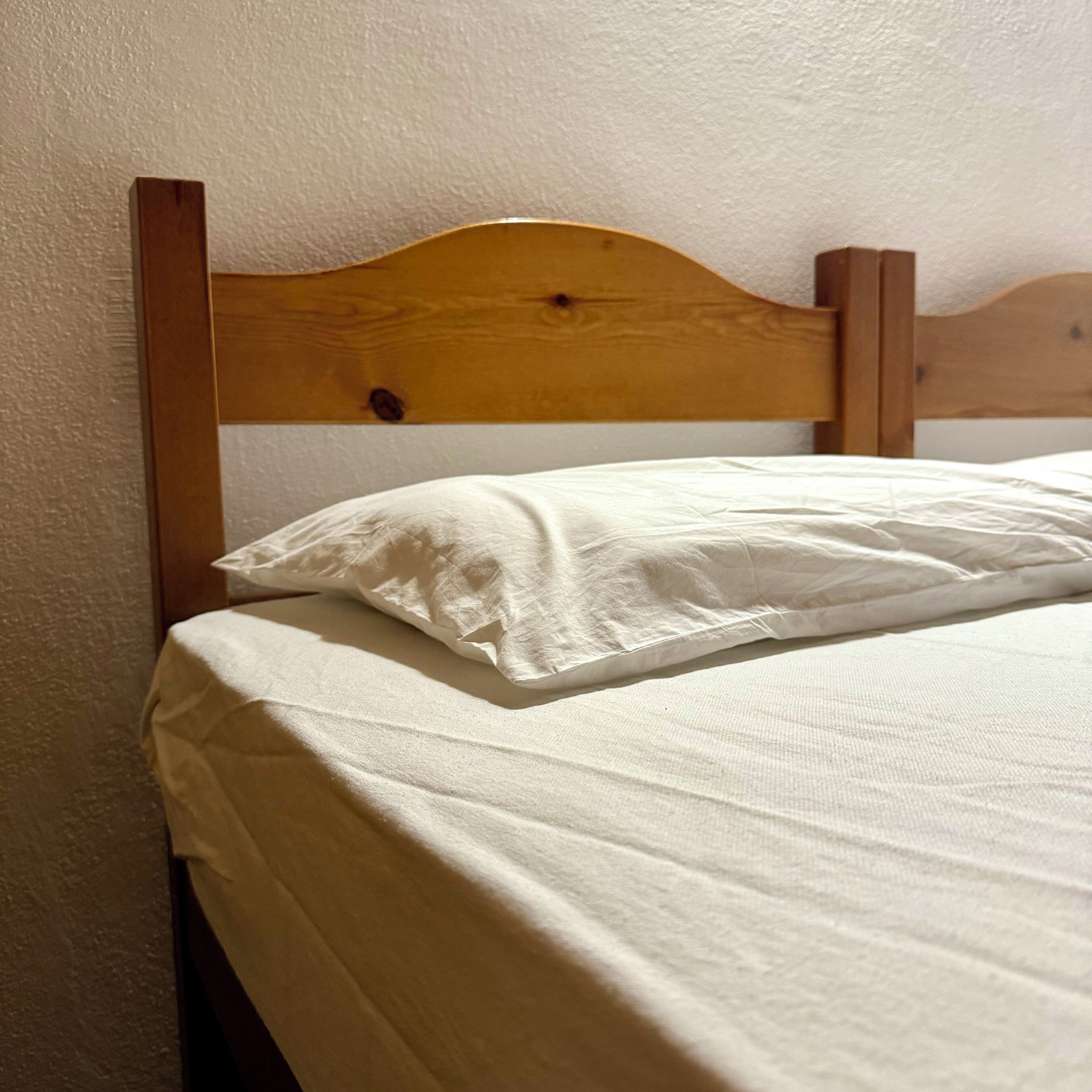 Un lit avec une tête de lit en bois et une literie blanche, dans une pièce aux murs texturés.