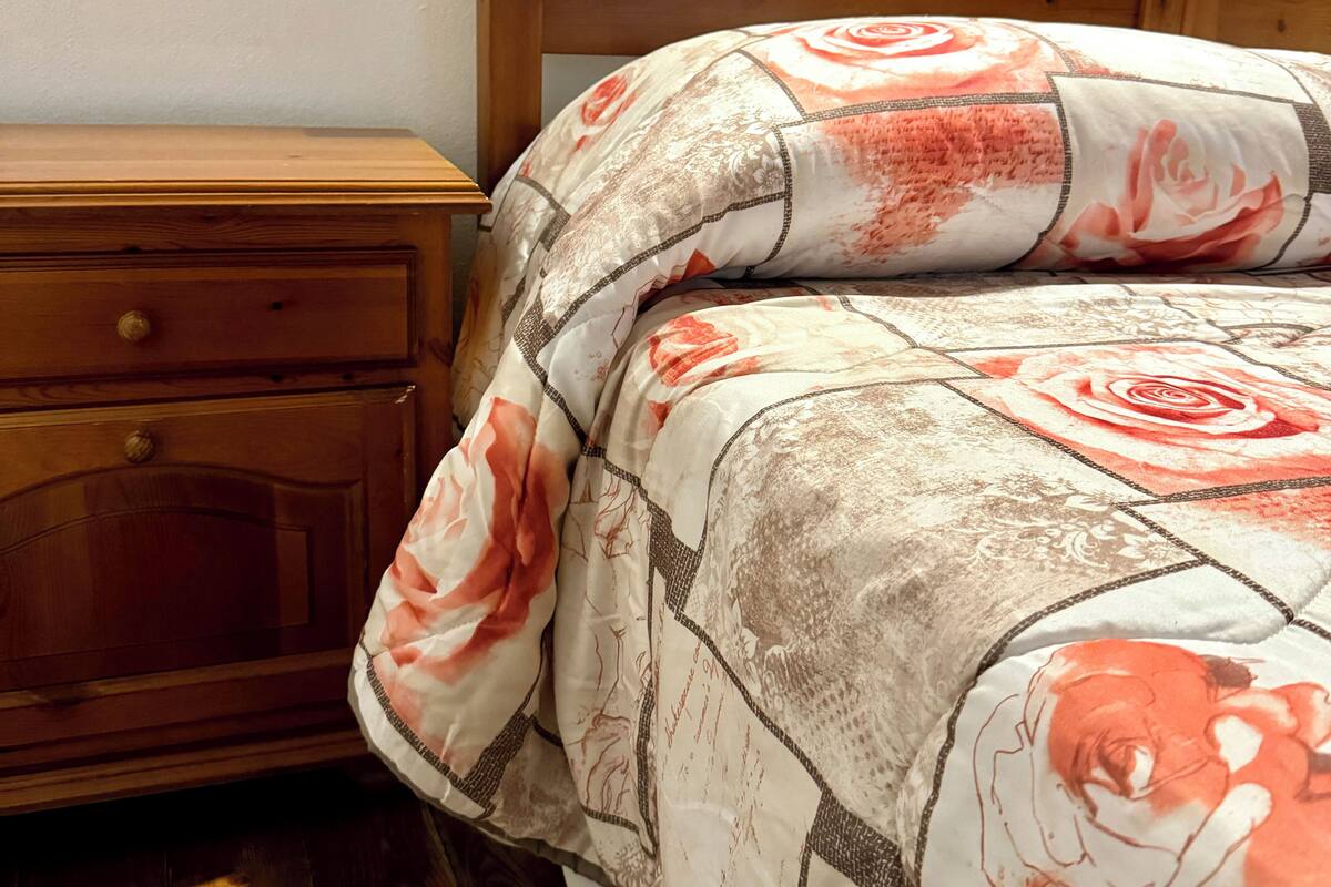 A bedroom with a wooden headboard, a wooden nightstand with a drawer, and a floral-patterned bedspread.