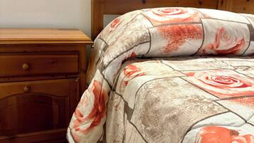 Camera da letto con testiera in legno, comodino in legno con un cassetto e copripiumino a motivi floreali.