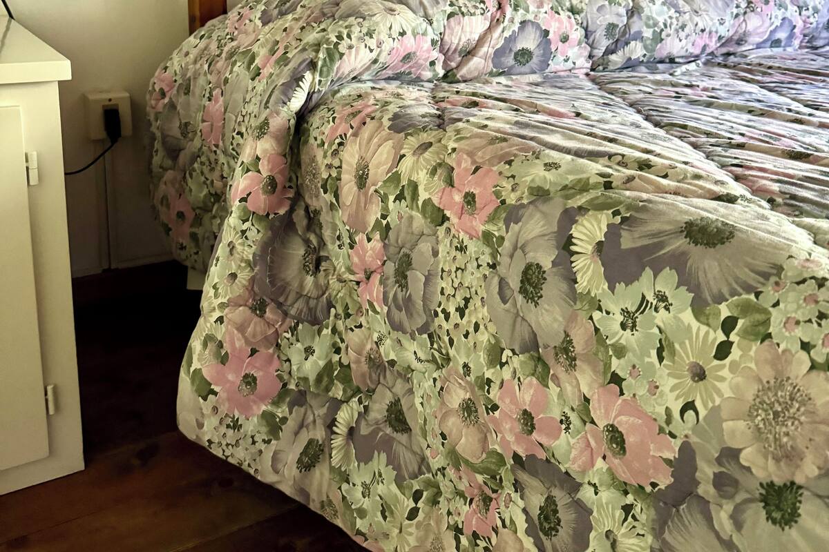 A bed with a floral bedspread, a wooden headboard, and a white bedside table.