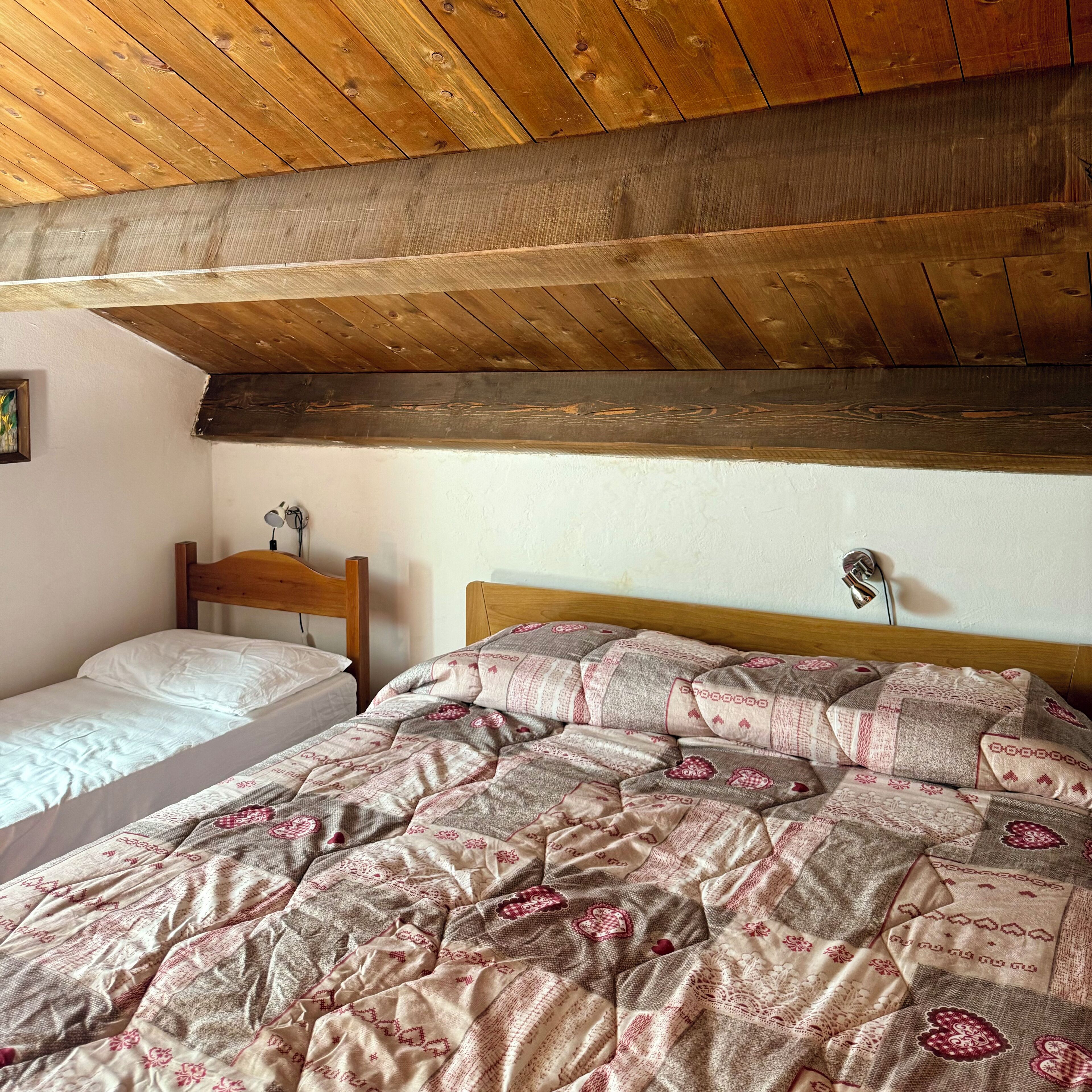 Un dormitorio con techo de madera, dos camas y una mesita de noche con lámpara.