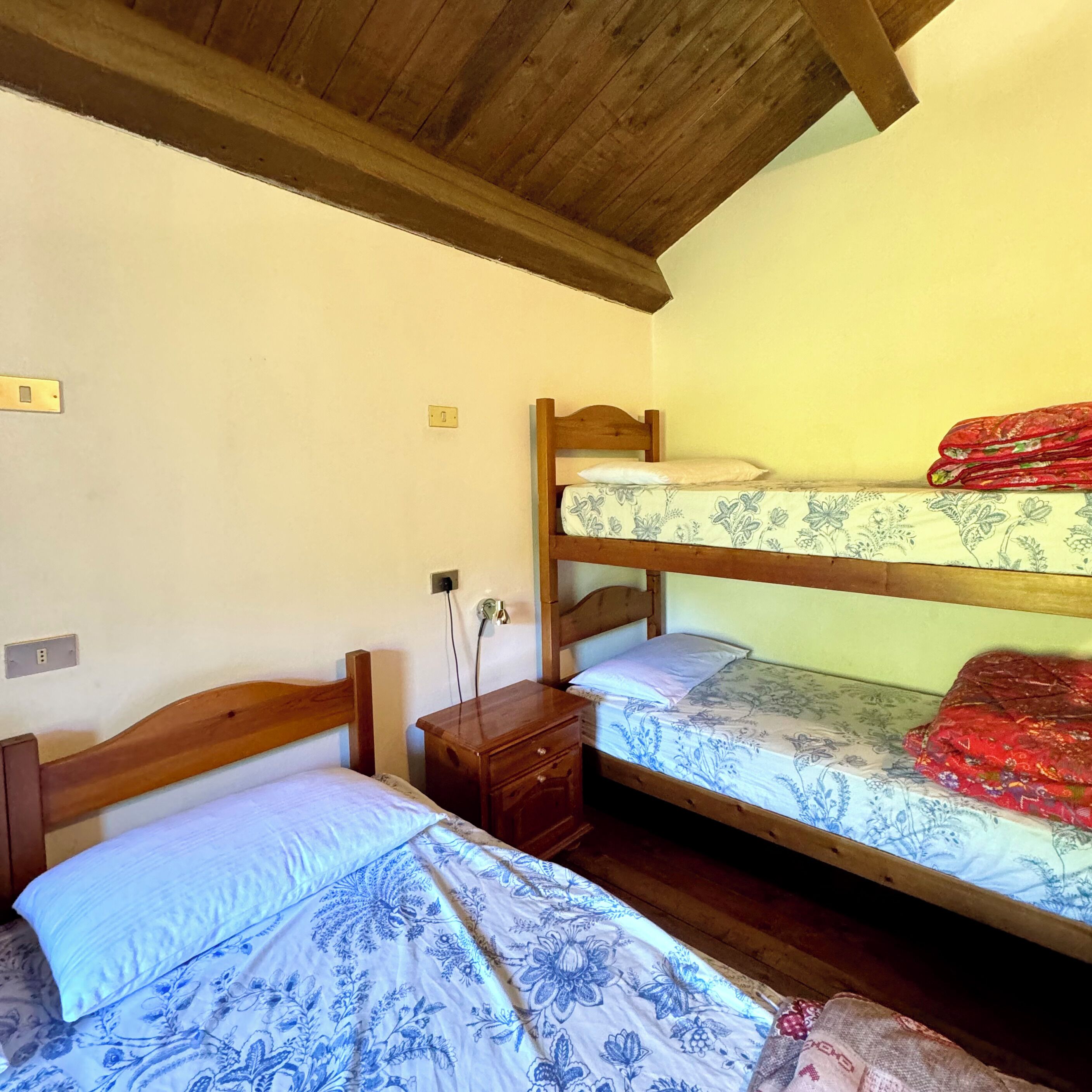 Une chambre avec deux lits superposés, une table de chevet en bois et une prise électrique au mur.